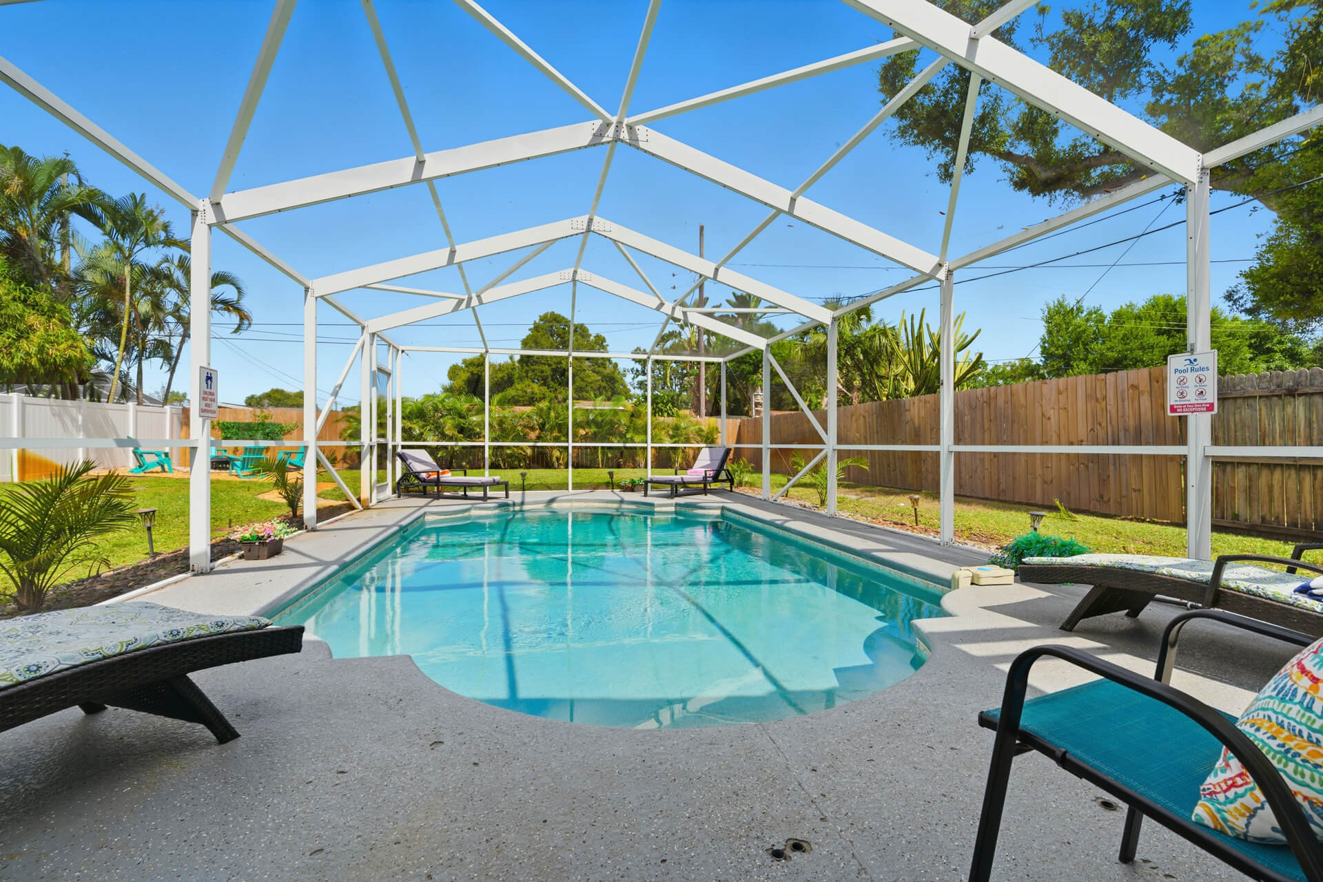 Screened-in private pool at Sun Oasis, a vacation rental in St. Petersburg, FL — crystal-clear water, lounge chairs, and lush tropical landscaping in a fully fenced backyard.