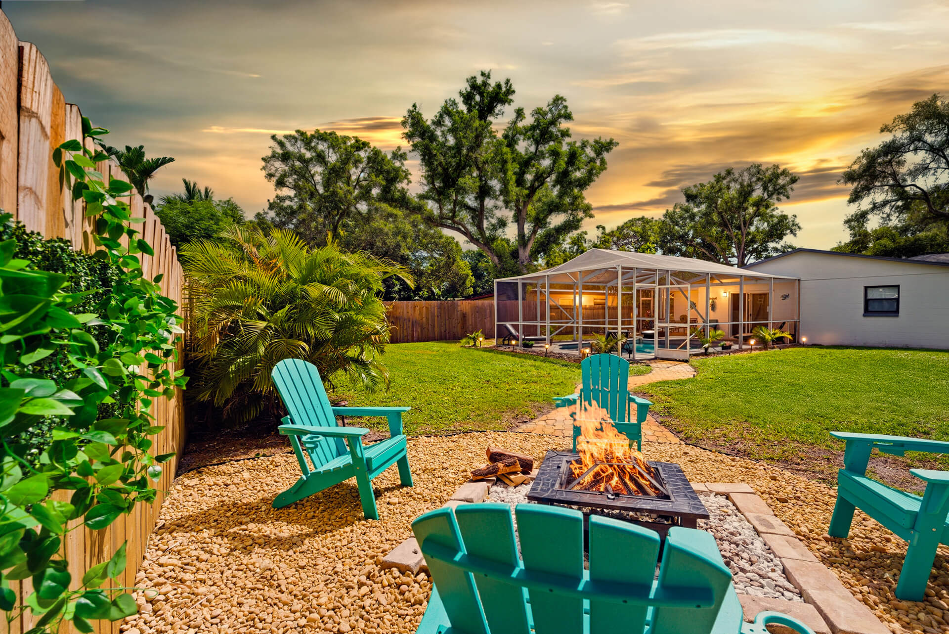 Golden-hour fire pit at Sun Oasis — teal Adirondack chairs, real wood flames, lush tropical palms, and a screened pool glowing in the background. The perfect Florida evening.